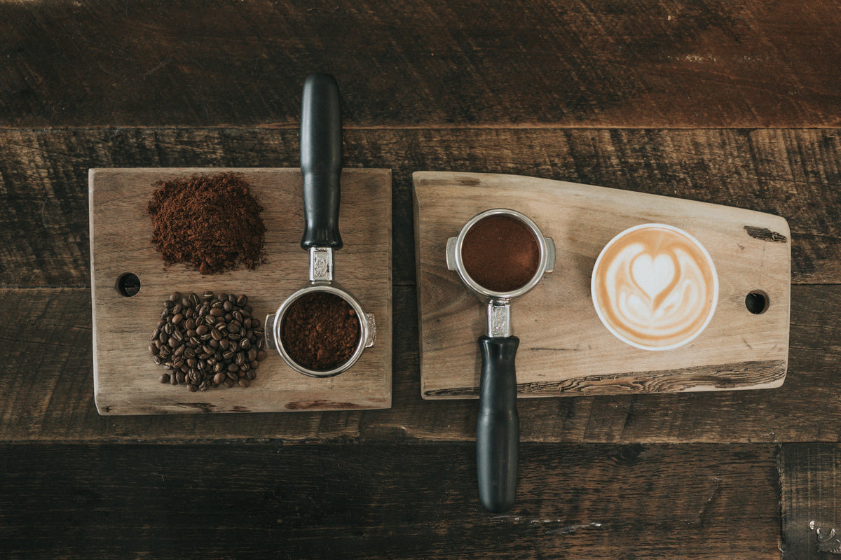 Image of coffee beans, ground coffee, espresso filters, and a latte on top of wooden serving trays